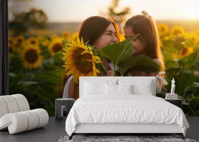 Beautiful young mom cuddling her young daughter among sunflowers at sunset. Motherly love, happy childhood. Wall mural