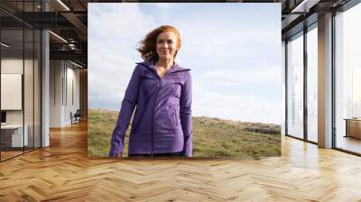 Beautiful red hair woman wearing purple jacket outside near beach Wall mural