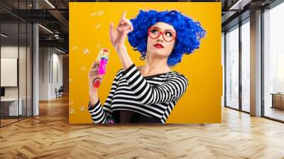 Cute girl wearing vibrant blue wig playing and blowing bubbles Wall mural