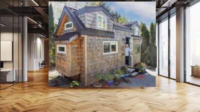 Friendly mature woman standing at front door of her charming little wooden tiny home or house Wall mural