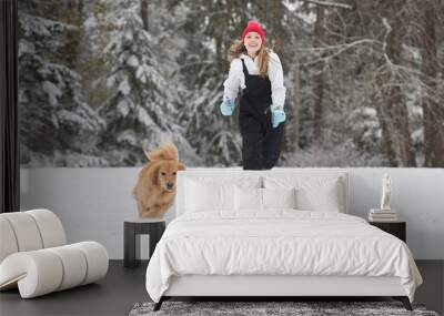 Happy young girl running in the snow with her golden retriever d Wall mural