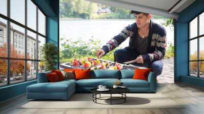 Man cooks vegetable kebab over fire pit Wall mural