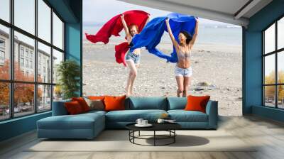 Two women playing with colorful fabric at the ocean beach Wall mural