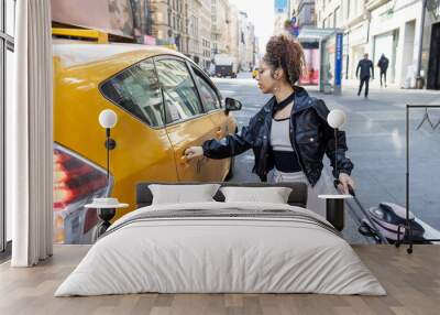 Young mixed race woman wearing black leather jacket in yellow taxi cab for city transportation Wall mural