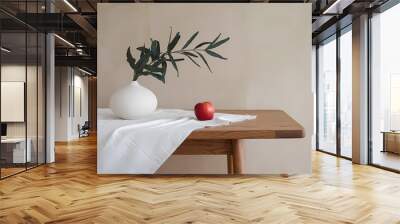 Minimalist decor featuring a white vase with greenery and a red apple on a wooden table, enhancing a serene home atmosphere. Wall mural