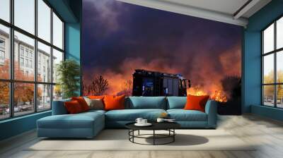 Team of fire fighters fighting fire in the evening. Fire truck on the flames and smoke background. Wall mural