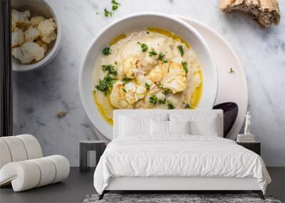 Roasted cauliflower cream soup on white kitchen table, served with fresh parsley, olive oil and bread. Overhead view. Wall mural