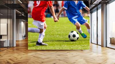 Boys play soccer. Teenagers playing soccer in sports field. Children kicking soccer game outdoors. Young male footballers running in red and blue sports uniforms Wall mural