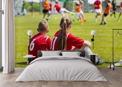 Soccer School Friends. Children soccer players playing game. Young girl and boy soccer players sitting together on grass football field.  Wall mural