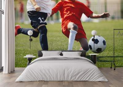 Sports players in football duel run. Footballers running fast and kicking soccer ball on grass stadium during school tournament match. Competition between defender and forward football players Wall mural