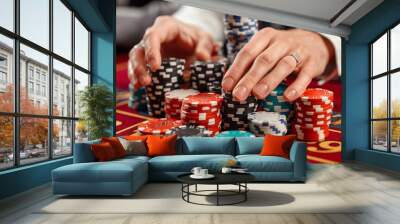 A close-up image of a hand placing a stack of colorful casino chips on a red felt table, representing the excitement of online gambling and betting Wall mural