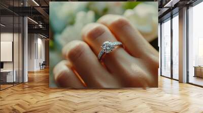 A close-up of a hand displaying an elegant engagement ring, surrounded by soft floral arrangements. Wall mural