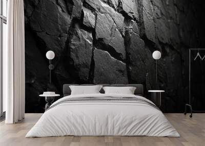 A close-up view of a textured black stone wall, emphasizing its rugged surface and shadows. Wall mural