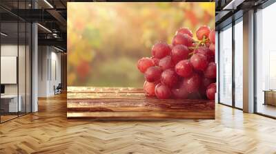 A cluster of fresh, dewy red grapes resting on a wooden surface, illuminated by soft sunlight in a natural setting. Wall mural