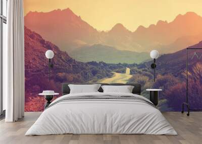 A serene dirt path winds through a mountainous landscape at sunset, creating a tranquil and inviting atmosphere. Wall mural