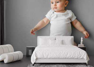 baby dressed in a plain white onesie lying on a smooth gray background, capturing the innocence and simplicity of early childhood in a soft, warm tone. Wall mural