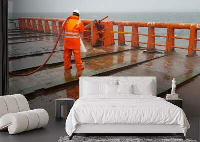 a sailor washes the deck of a ship with the pressure of sea water from a fire hose Wall mural