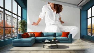 Young woman in white shirt on white background. Beautiful girl in white clothes sits on the floor on a white background. Studio shot. Wall mural