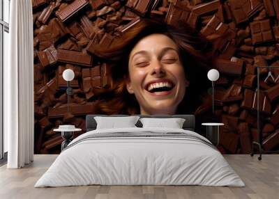 Portrait of a happy laughing young woman laying on top of a pile of delicious chocolate bars. Wall mural