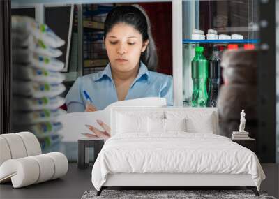 young woman, working in a store, organizing and writing down a list of existing products. Wall mural