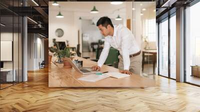 Asian businessman leaning over his desk working with a laptop Wall mural