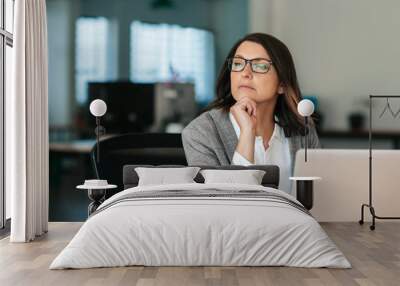 Businesswoman thinking about work while sitting at her office desk Wall mural