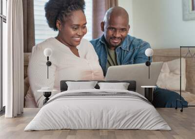 Smiling African couple sitting on a sofa using a laptop Wall mural