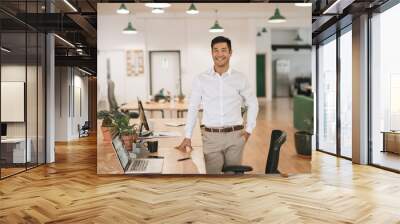 Smiling Asian businessman standing by his desk in an office Wall mural