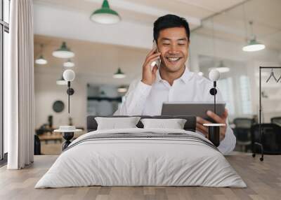 Smiling Asian businessman using a cellphone and tablet at work Wall mural