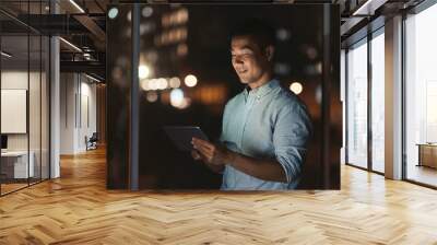 Smiling Asian businessman using a tablet late at night Wall mural