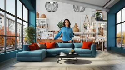 Smiling Asian entrepreneur standing by a counter in her store Wall mural