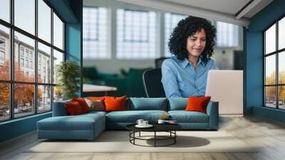 Smiling businesswoman sitting at her desk working on a laptop Wall mural