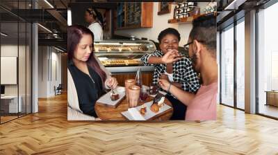 Smiling friends sitting at a cafe table eating desserts together Wall mural