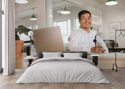 smiling young asian businessman working alone at his office desk Wall mural