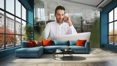 Smiling young businessman talking on a cellphone at work Wall mural