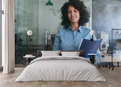 Smiling young businesswoman carrying paperwork while standing in an office  Wall mural