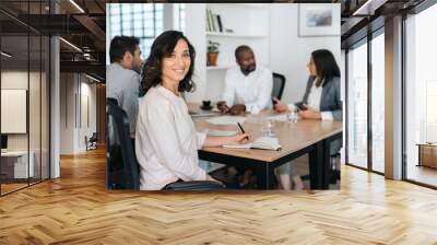 Smiling young businesswoman sitting with coworkers during a meeting Wall mural