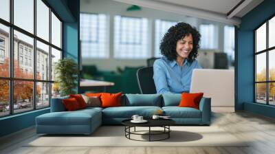 Smiling young businesswoman working on a laptop at her desk Wall mural