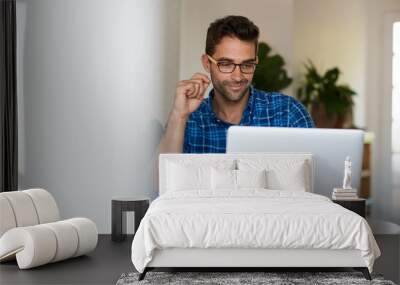 Smiling young man working online with a laptop from home Wall mural