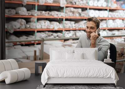 Warehouse manager sitting at his desk talking on a cellphone Wall mural