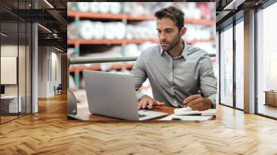 Warehouse manager taking notes and checking orders with a laptop Wall mural