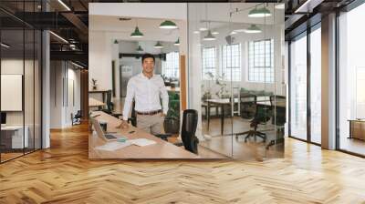 Young Asian businessman smiling while standing by his office desk Wall mural