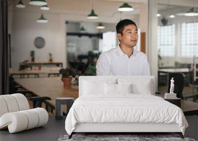 Young Asian businessman standing in an office deep in thought Wall mural