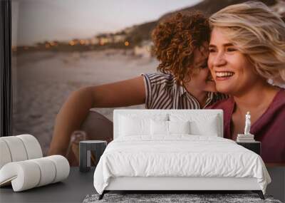 Young lesbian couple having drinks while watching a beach sunset Wall mural