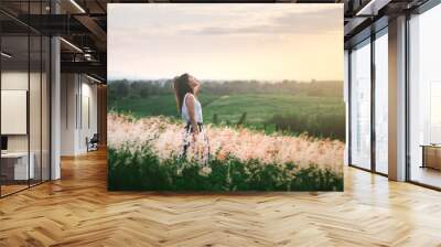 Trendy girl in stylish summer dress feeling free in the field with flowers in sunshine. Wall mural