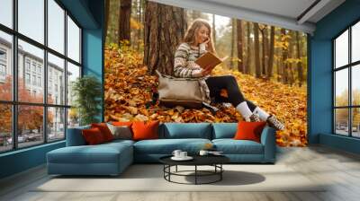 A young woman enjoys a quiet moment, immersed in a book while seated on colorful fallen leaves. . Education. Concept of enjoying nature. Wall mural