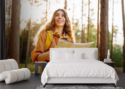 A young woman explores a forest while reading a map in the sunlight, enjoying a beautiful day outdoors Wall mural