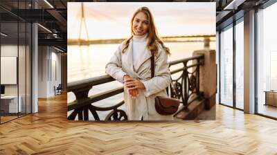 A young woman walks along the embankment and enjoys the warm autumn sunset. Lifestyle, travel, tourism, active life. Wall mural