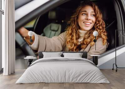 A young woman with curly hair smiling while driving a car in a city during daytime on a clear sunny day Wall mural