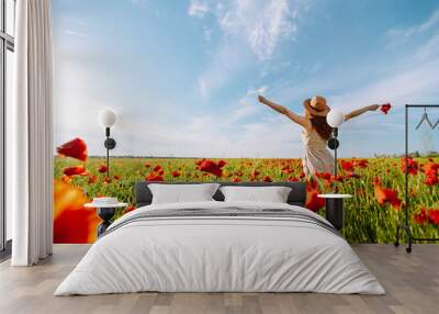 Back view. Young curly woman  in hat posing in the poppy field. Nature, vacation, relax and lifestyle. Summer landscape. Wall mural